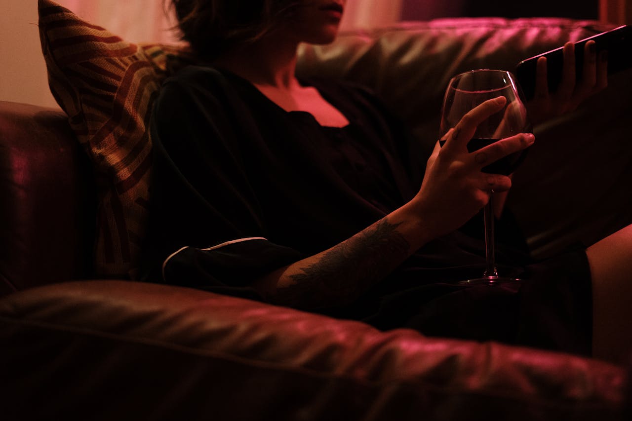 A woman relaxing on a couch with a glass of wine, enveloped in warm ambient lighting.